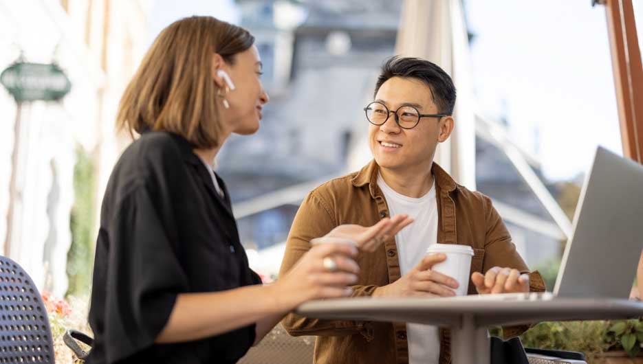 Multiracial business people talking and working with laptop in cafe. Concept of remote and freelance work. Idea of teamwork and business cooperation. Caucasian woman and asian man drinking coffee