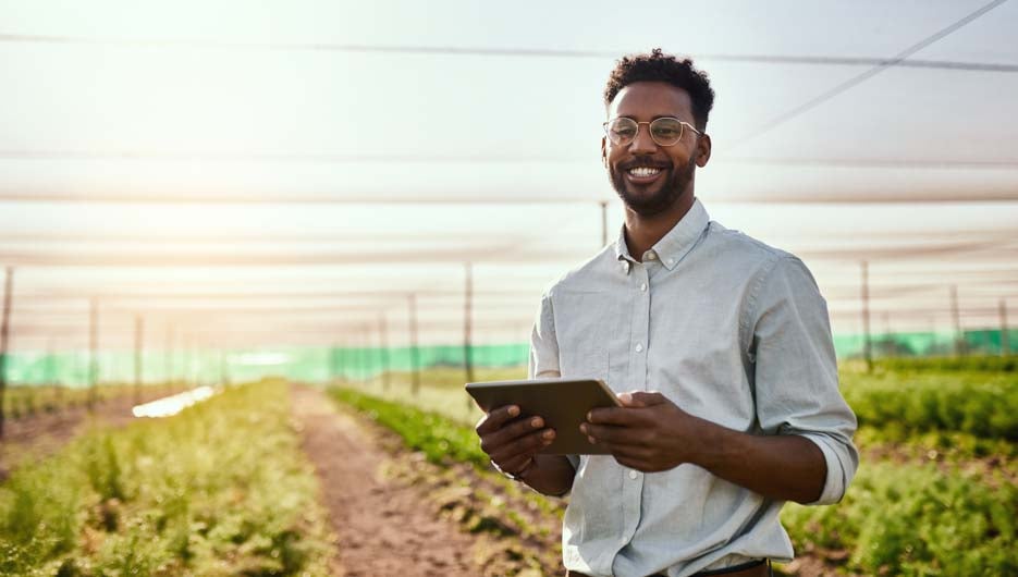 Young African male farmer working on healthy agriculture development strategy on his digital tablet. Smiling field worker outdoors on organic farming and growth sustainability check up.