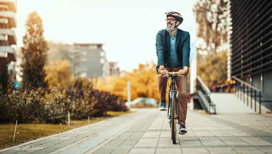 A handsome casual middle-aged businessman is going to the office by bicycle. He is driving bike in front of office district.